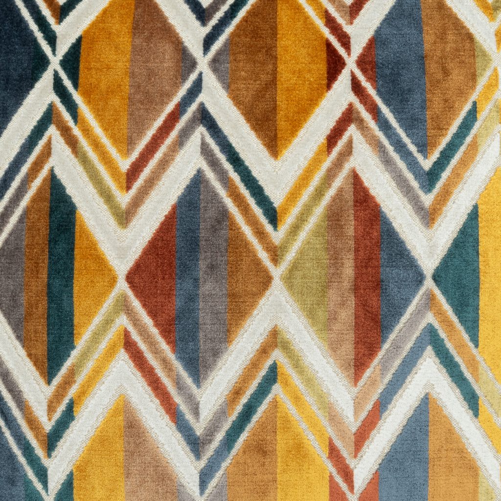 A close-up of a textured area rug featuring a geometric chevron and diamond pattern in mustard yellow, rust red, slate blue, teal, and cream.