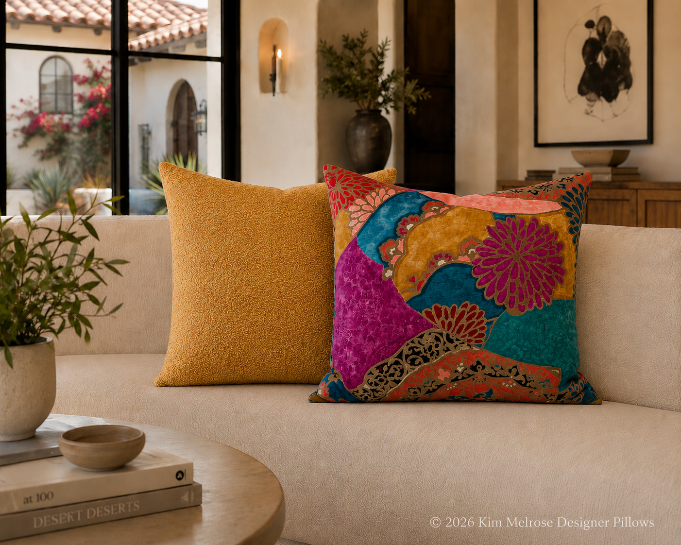 Two decorative throw pillows on a cream-colored sofa in a styled living room. One pillow is a solid textured mustard yellow, and the other is a vibrant, multicolored patchwork design with pink, teal, orange, and gold floral and abstract patterns.