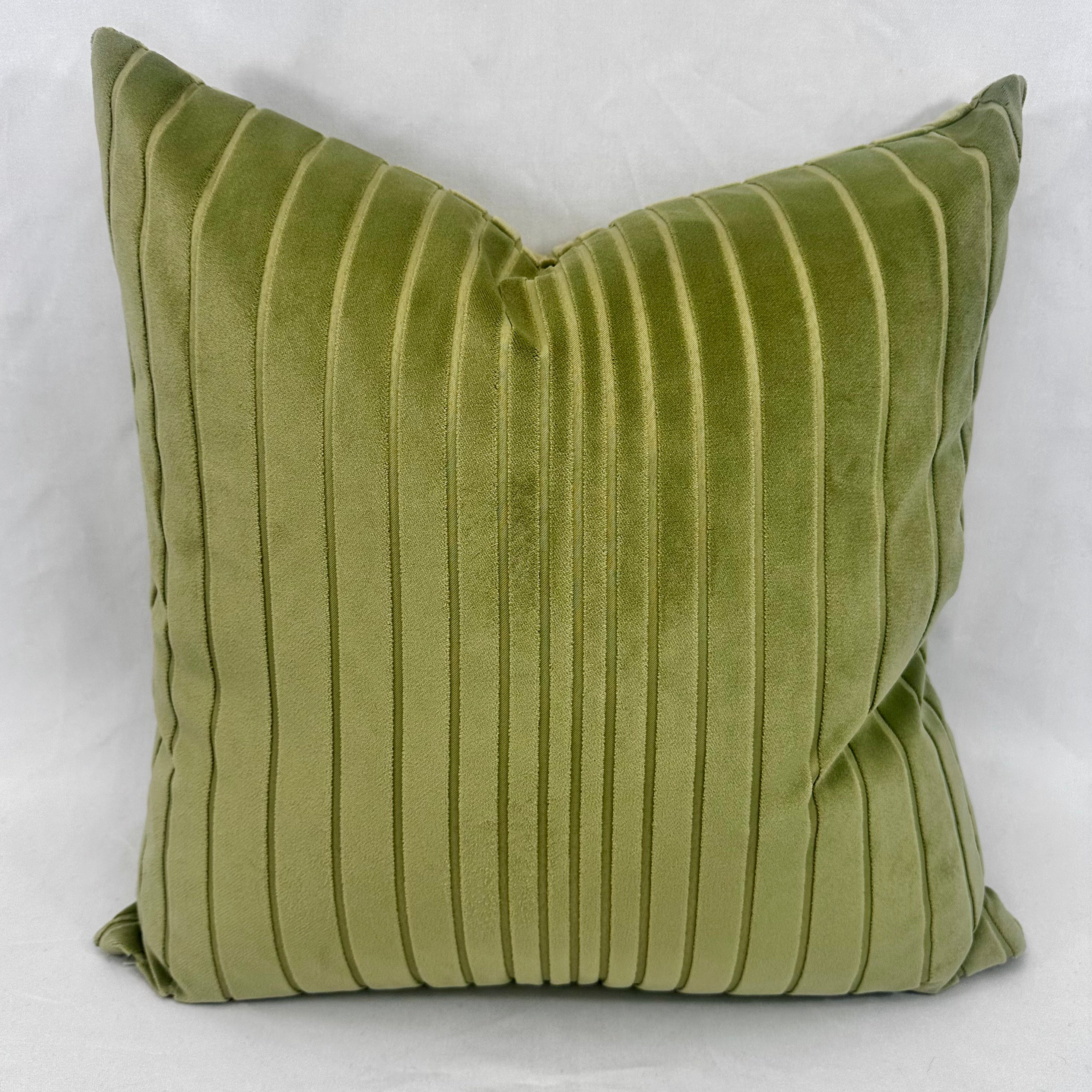 An olive green velvet square throw pillow with vertical channel tufting, shown against a light gray fabric background.