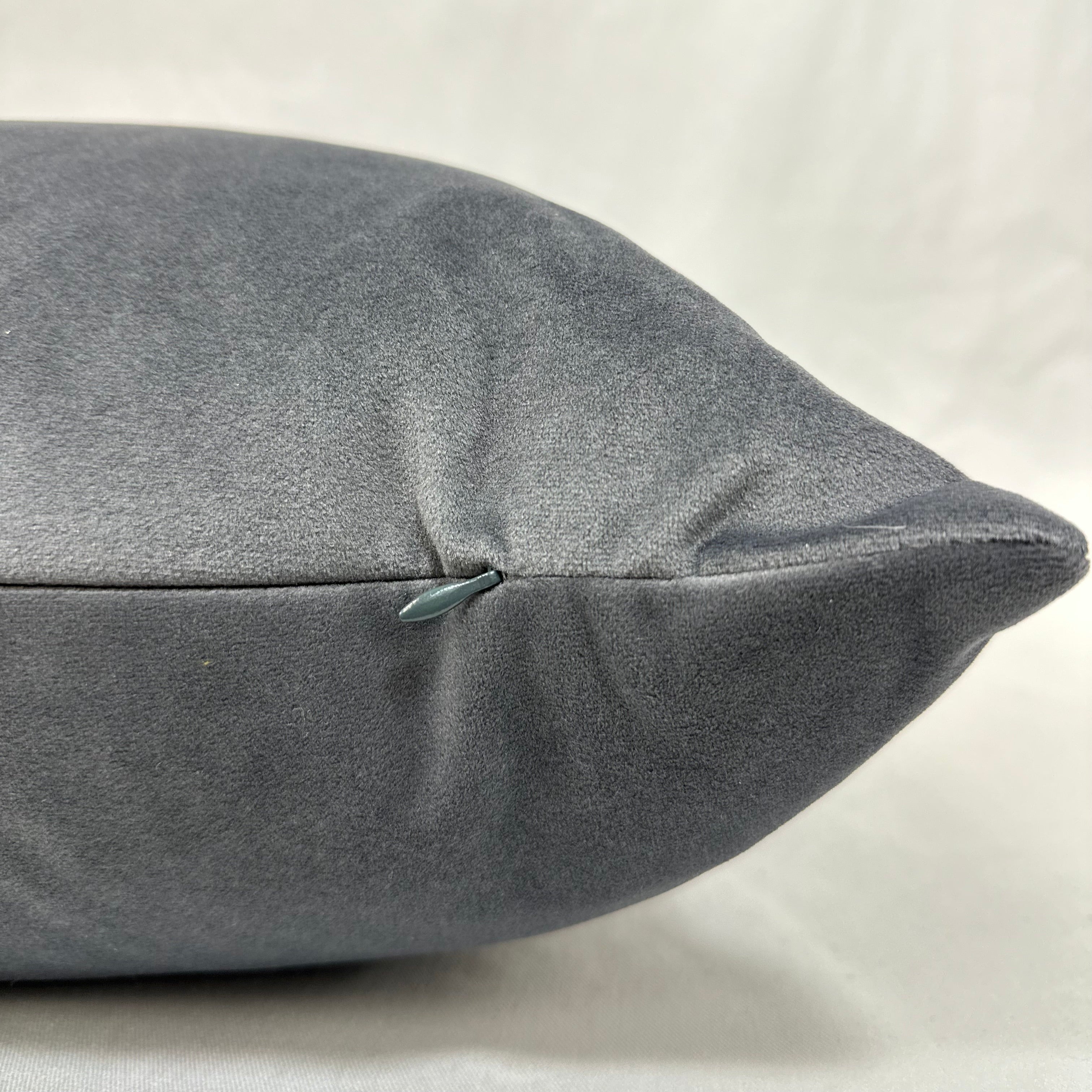 A close-up of a gray textured pillow or cushion corner with a visible zipper, set against a light neutral fabric background.