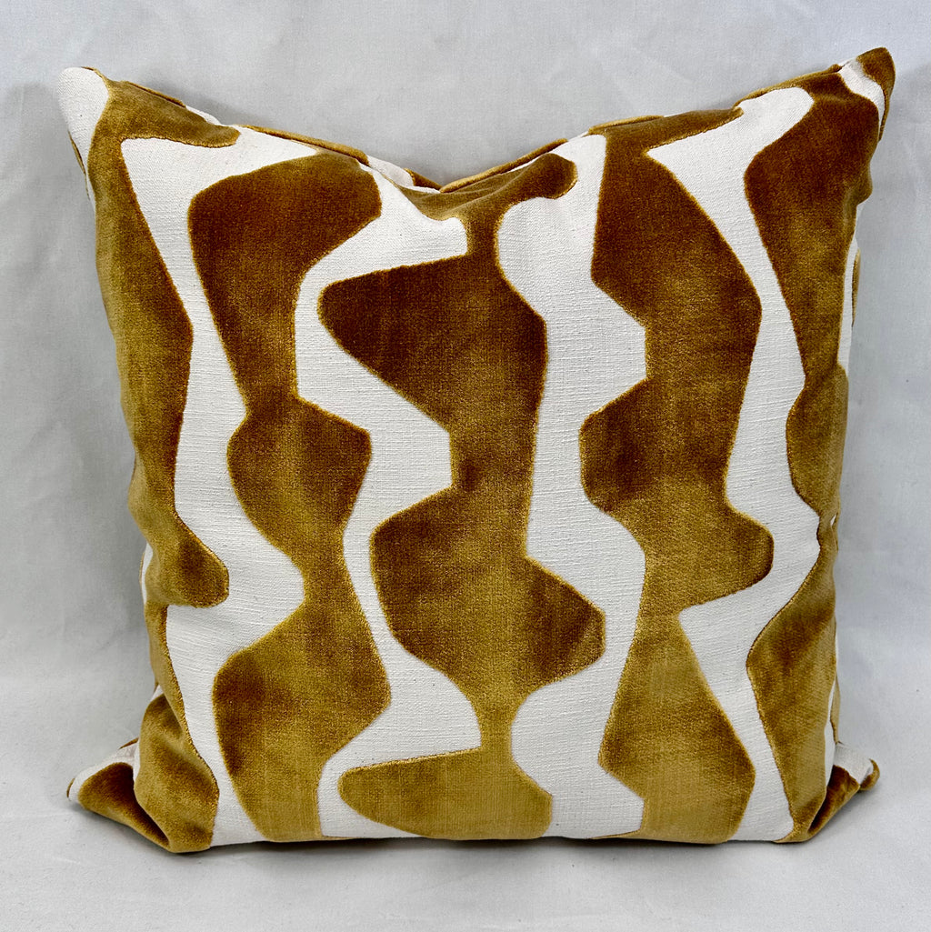 A square throw pillow featuring an abstract wavy pattern in mustard yellow velvet and off-white textured fabric, set against a neutral gray background.