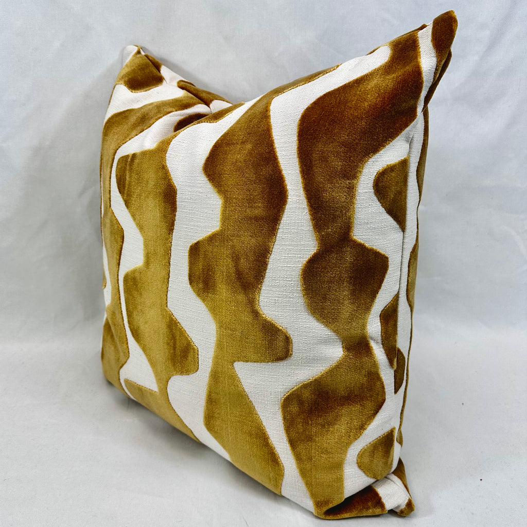 A square throw pillow featuring a bold, wavy abstract pattern in mustard yellow and white, photographed against a neutral light gray fabric backdrop.