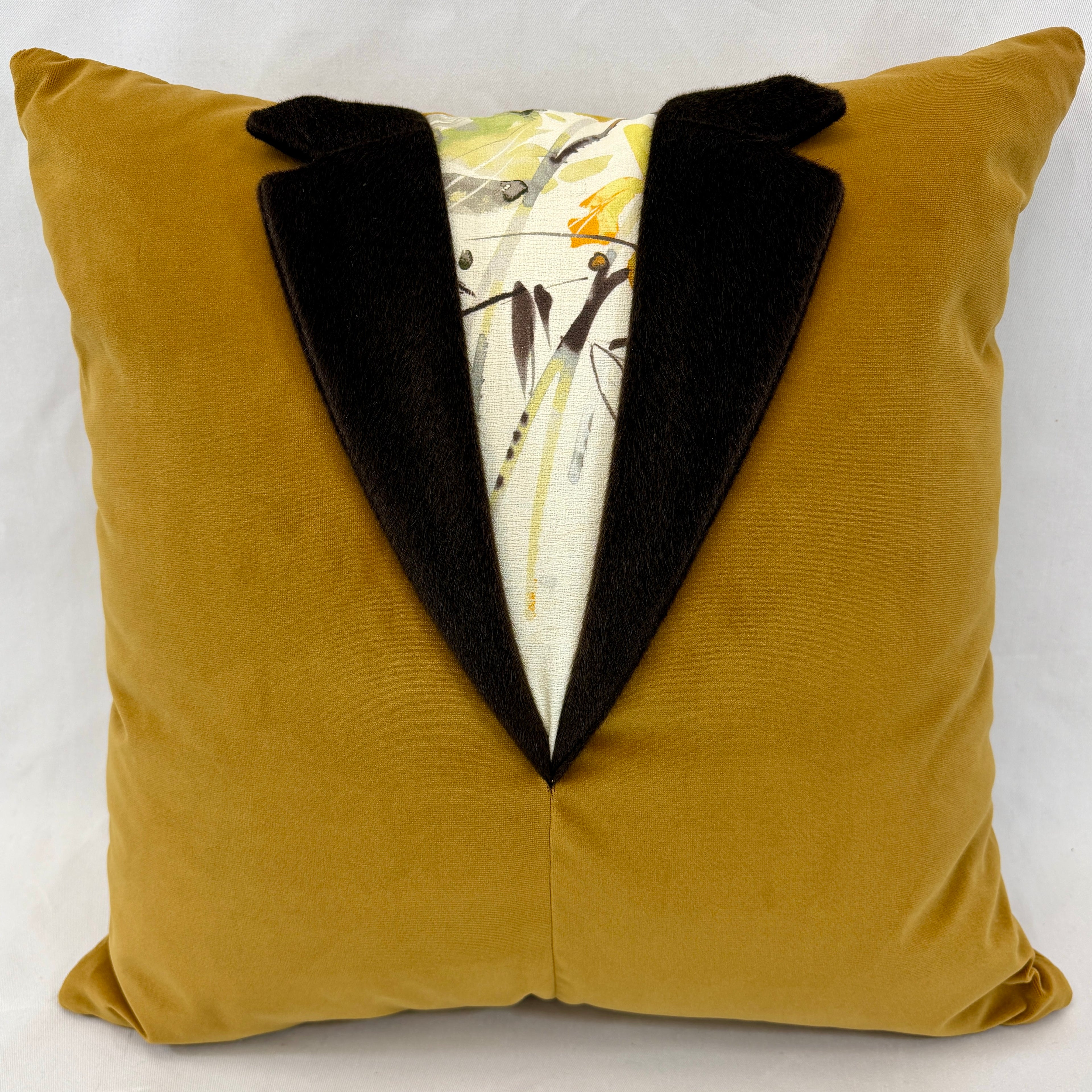A square decorative throw pillow in mustard yellow velvet with a black velvet tuxedo collar and a printed tuxedo lapel insert featuring a white background with abstract black and yellow brushstrokes.