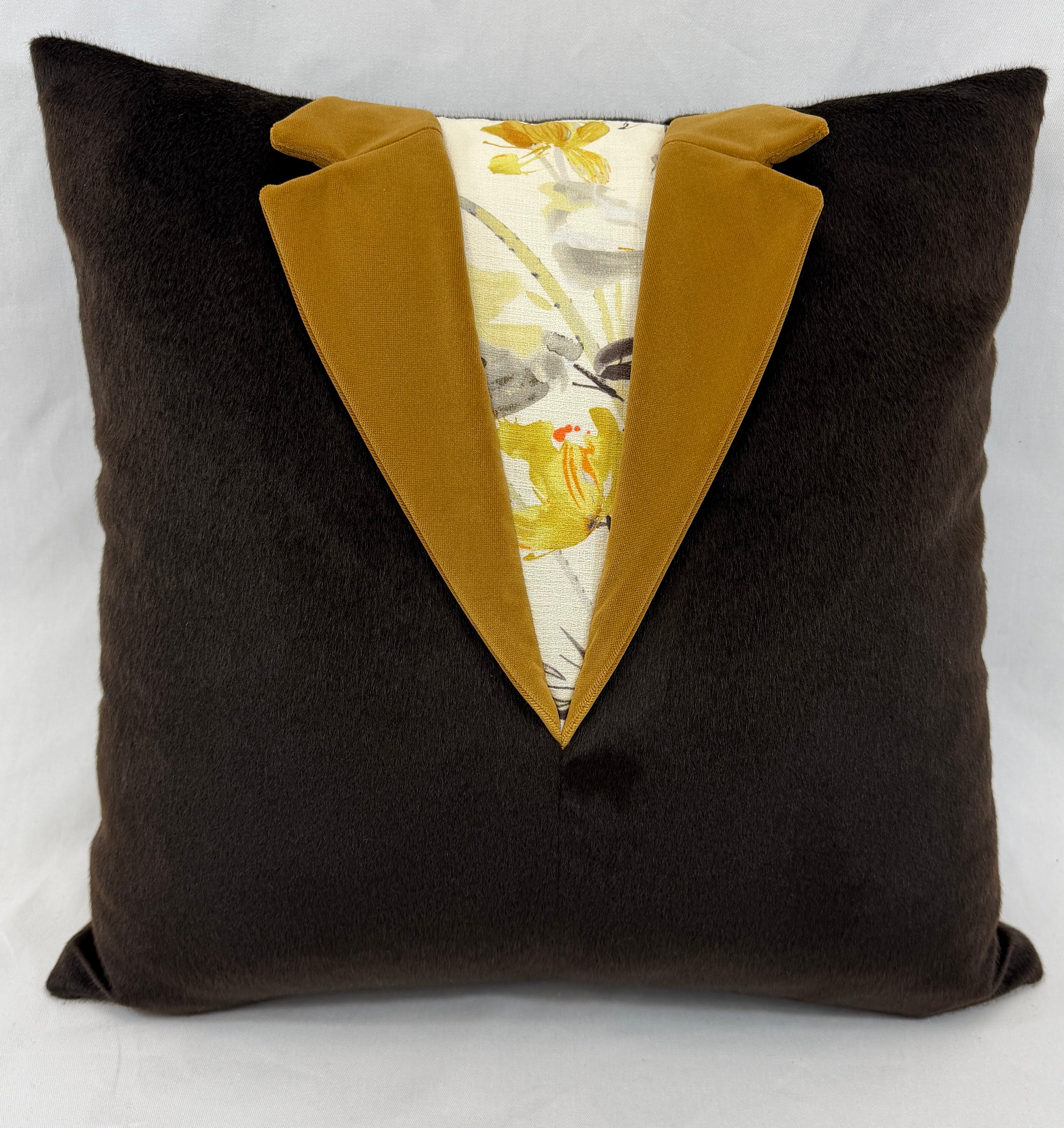 A square dark brown plush throw pillow designed to look like a tuxedo jacket, featuring mustard yellow satin lapels and a cream-colored center panel with a yellow and gray floral pattern.