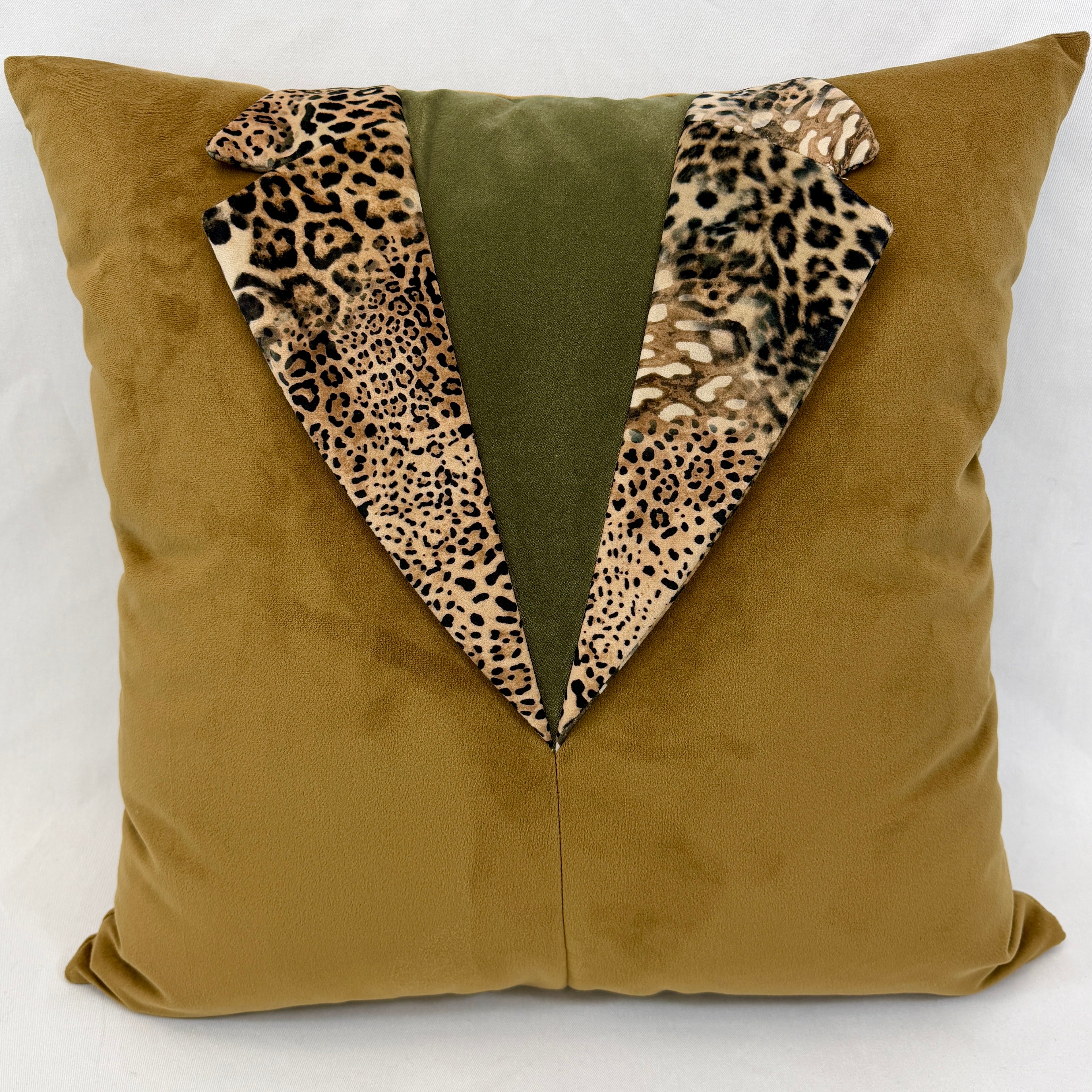 A square throw pillow in a textured mustard-yellow fabric, designed to look like a tuxedo jacket with a central olive green panel and leopard-print lapels.
