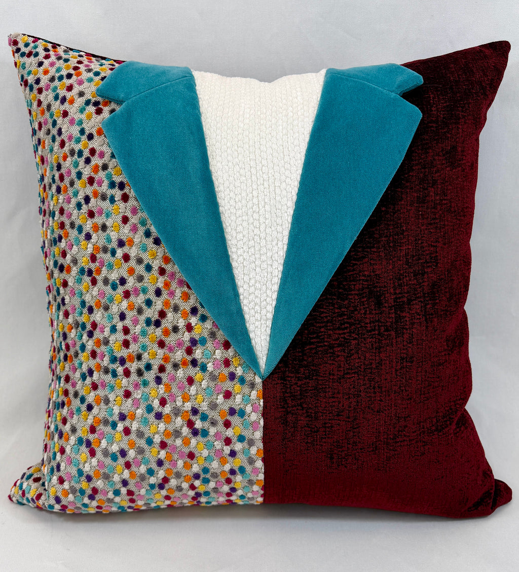 A square decorative throw pillow with a tuxedo-inspired design, featuring a multicolor speckled pattern on one side, a solid deep burgundy velvet side, and a teal velvet lapel with a white knit center front.