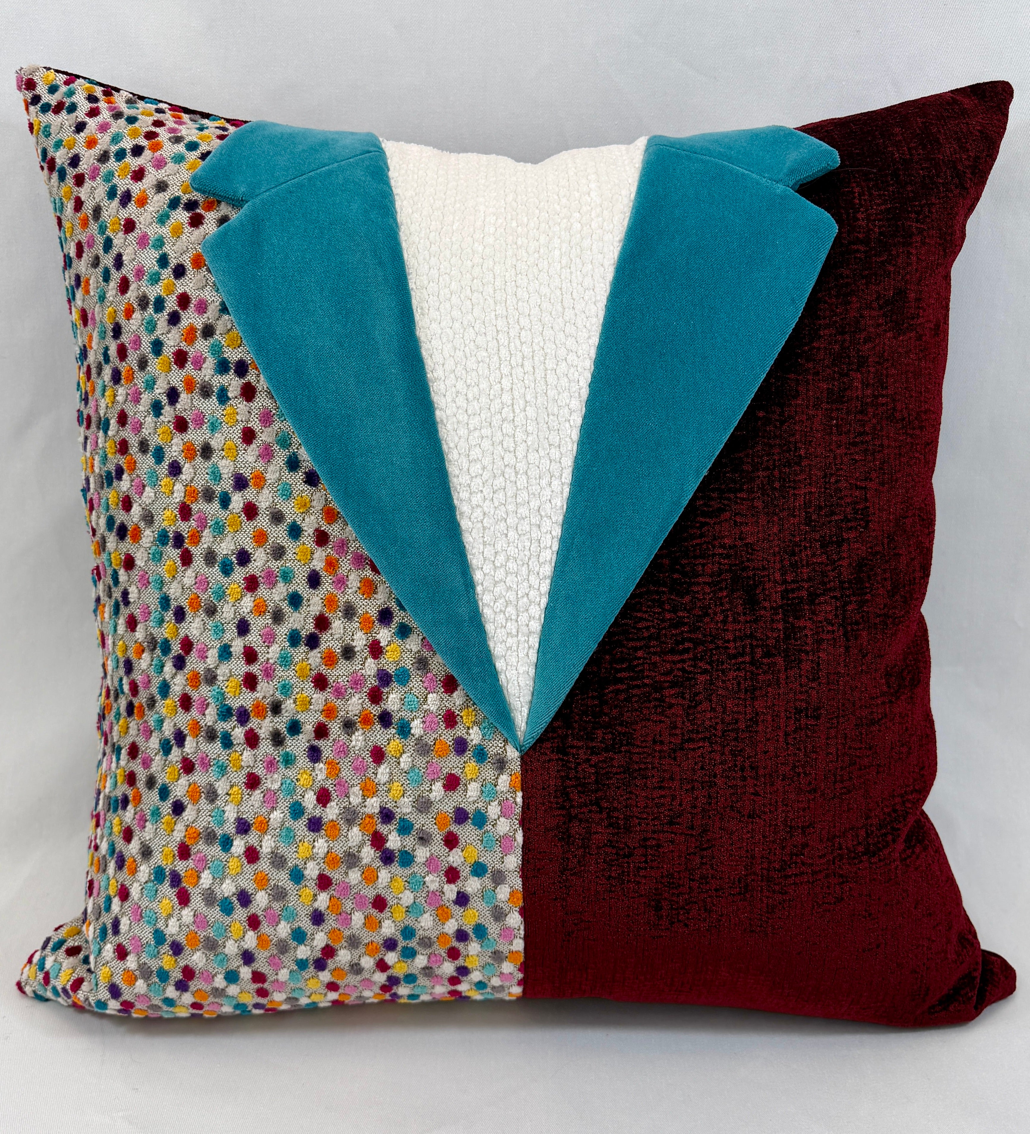 A square decorative throw pillow with a tuxedo-inspired design, featuring a multicolor speckled pattern on one side, a solid deep burgundy velvet side, and a teal velvet lapel with a white knit center front.