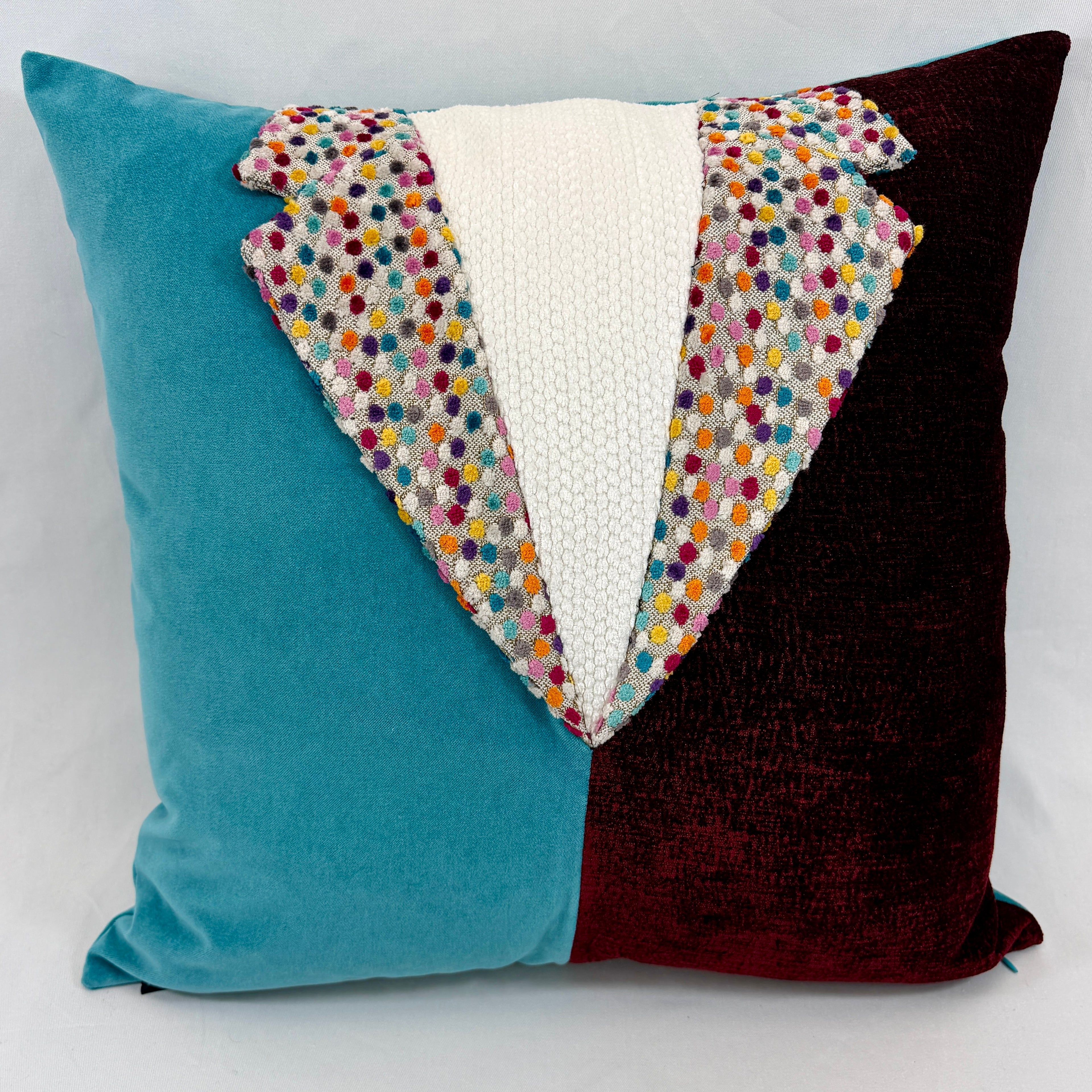 A square decorative throw pillow with a velvet-like split design in teal blue on the left and deep burgundy on the right, featuring a central white textured panel and a colorful embroidered polka-dot border.