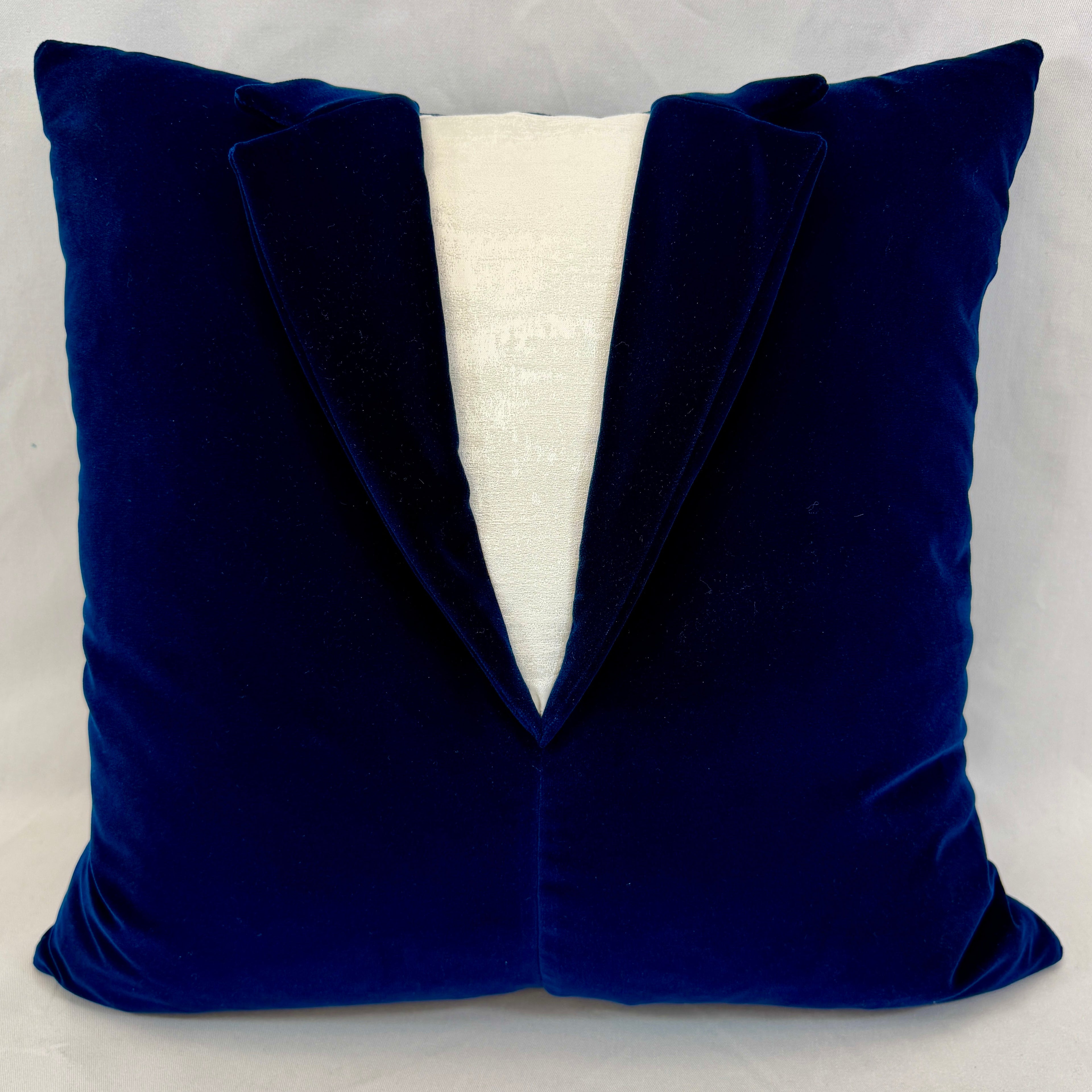 A square throw pillow designed to look like a velvet tuxedo jacket, featuring a deep royal blue body with a white textured V-shaped center panel.