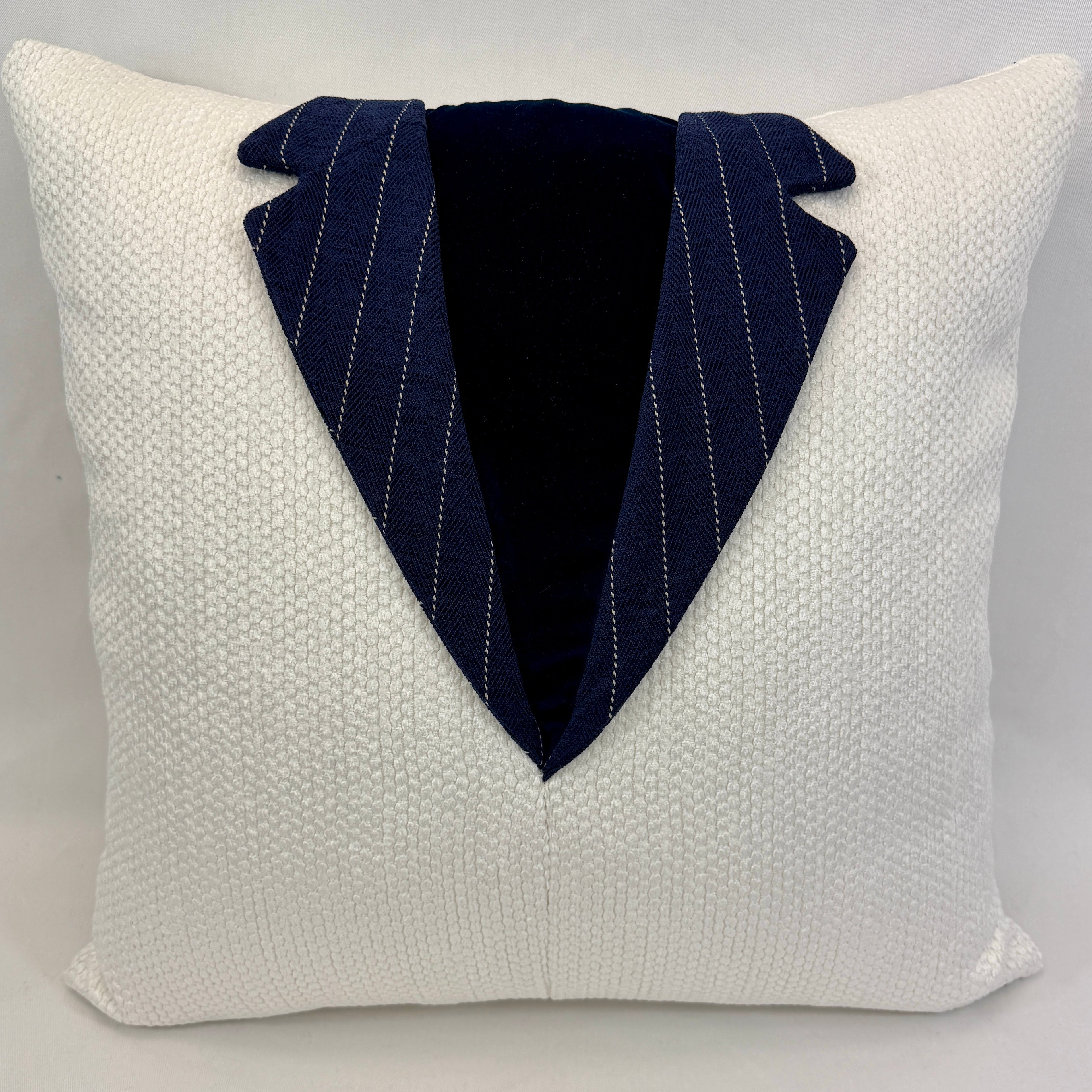 A square white textured throw pillow designed to look like a tuxedo jacket, featuring a dark navy blue pinstriped lapel and a black velvet inner placket.