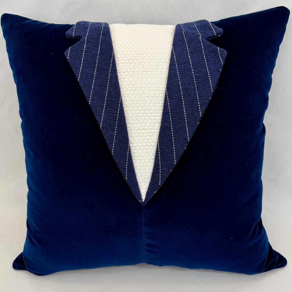A square navy blue velvet throw pillow designed to look like a tuxedo jacket, featuring a white textured center panel and pinstriped lapels.