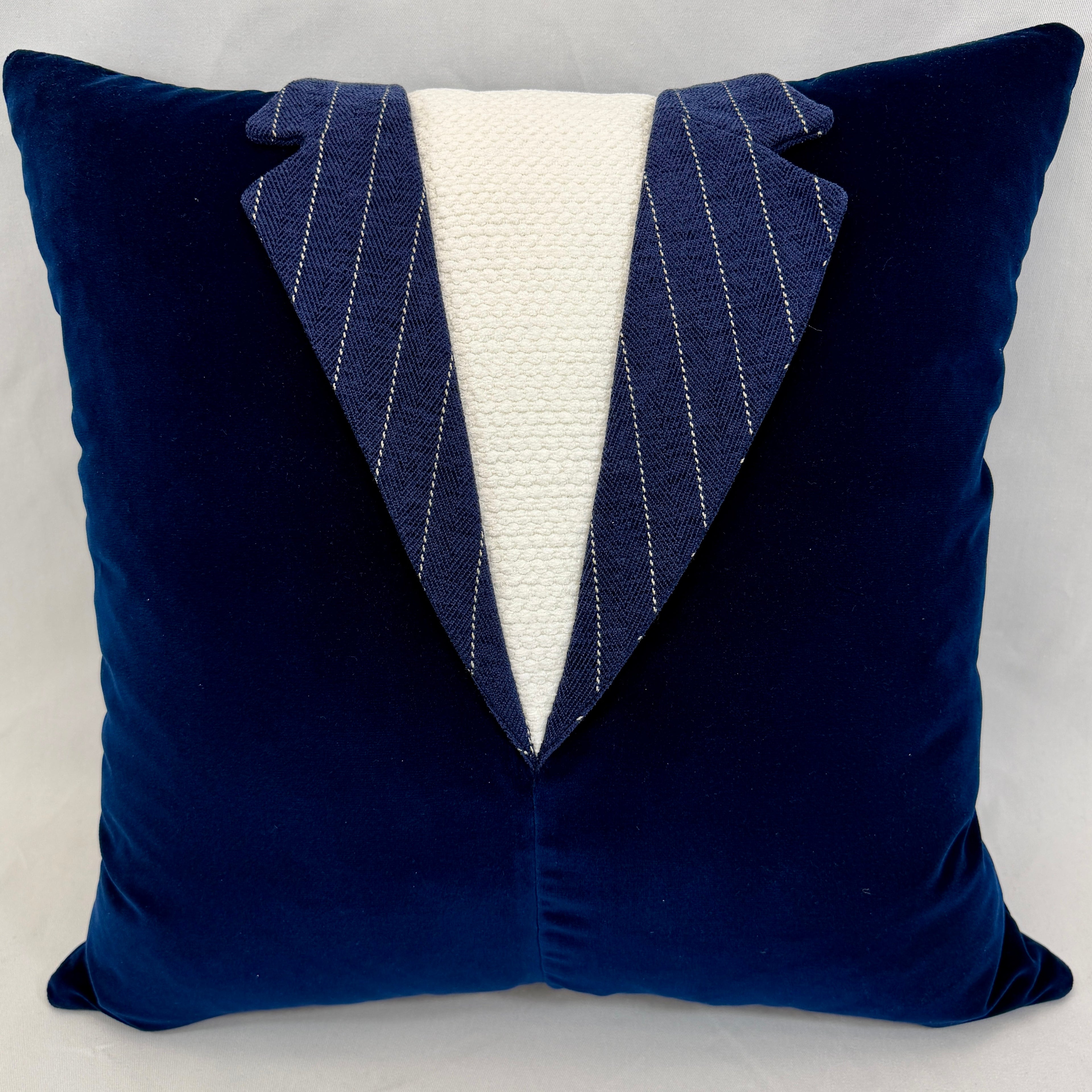 A square navy blue velvet throw pillow designed to look like a tuxedo jacket, featuring a white textured center panel and pinstriped lapels.
