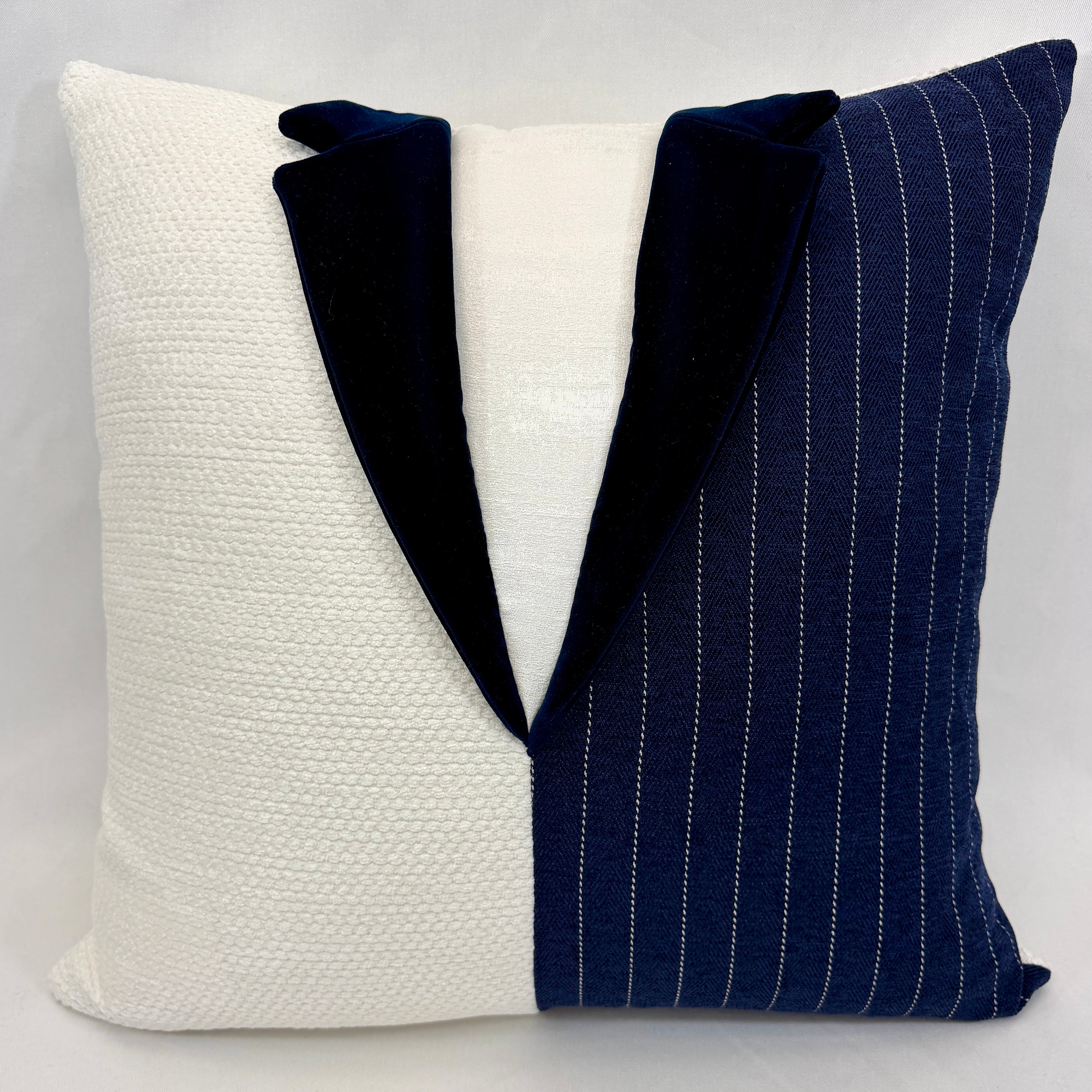 A square decorative throw pillow designed to look like a tuxedo jacket, featuring a textured off-white left side, a navy blue pinstripe right side, and a solid navy velvet lapel.
