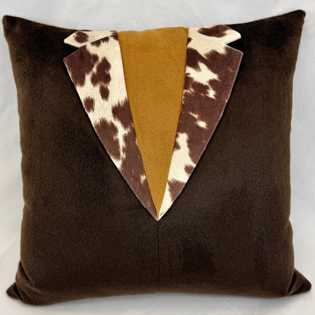 A square brown plush throw pillow designed to look like a tuxedo jacket, featuring a central mustard yellow faux-suede panel and a V-shaped lapel design in brown and cream cowhide print.