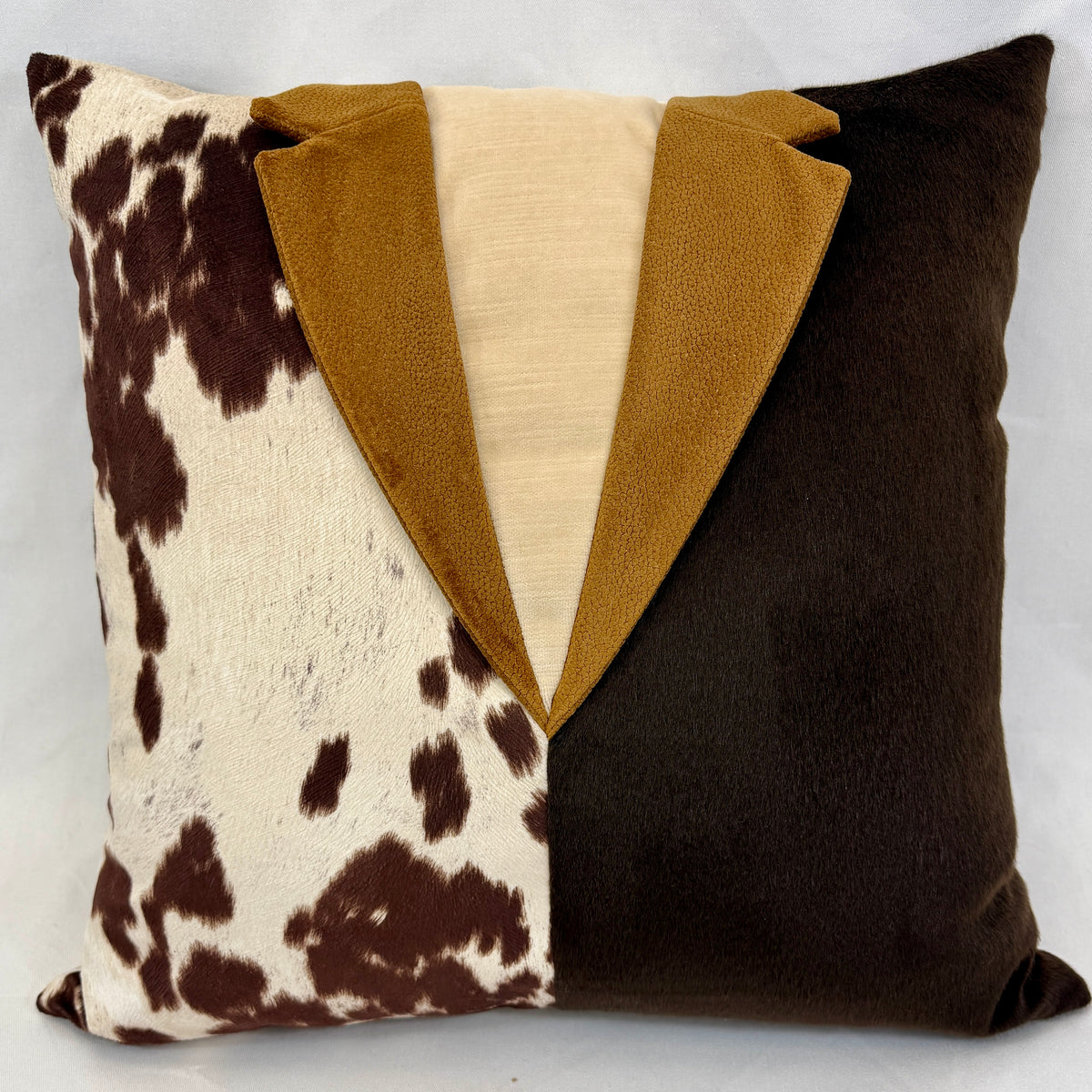A square decorative throw pillow featuring a split design: one half is brown and white cowhide print, the other half is solid dark brown, with a central faux-tie detail in camel brown and cream.