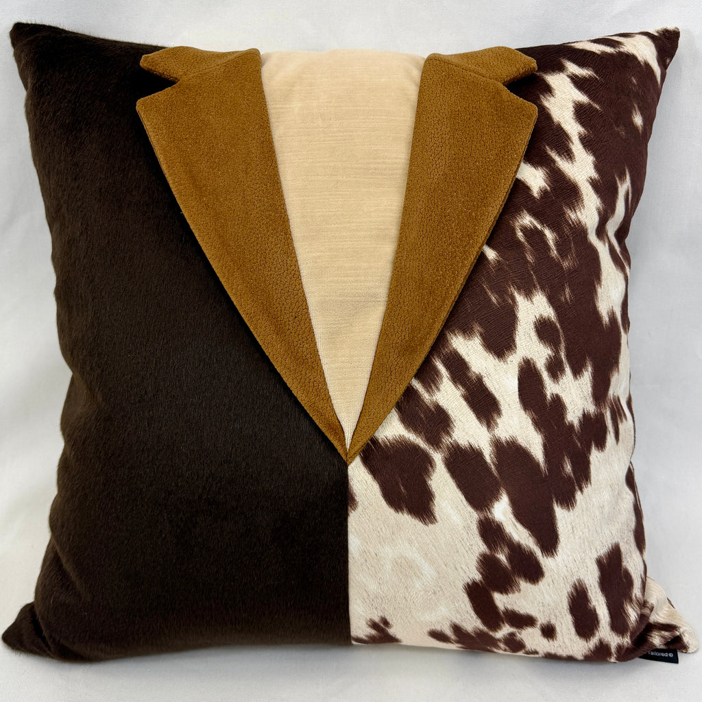 A square decorative throw pillow featuring a tuxedo-inspired design with a dark brown velvet lapel, a mustard brown velvet lapel, a cream center panel, and a brown-and-cream cow-print pattern on the right side.