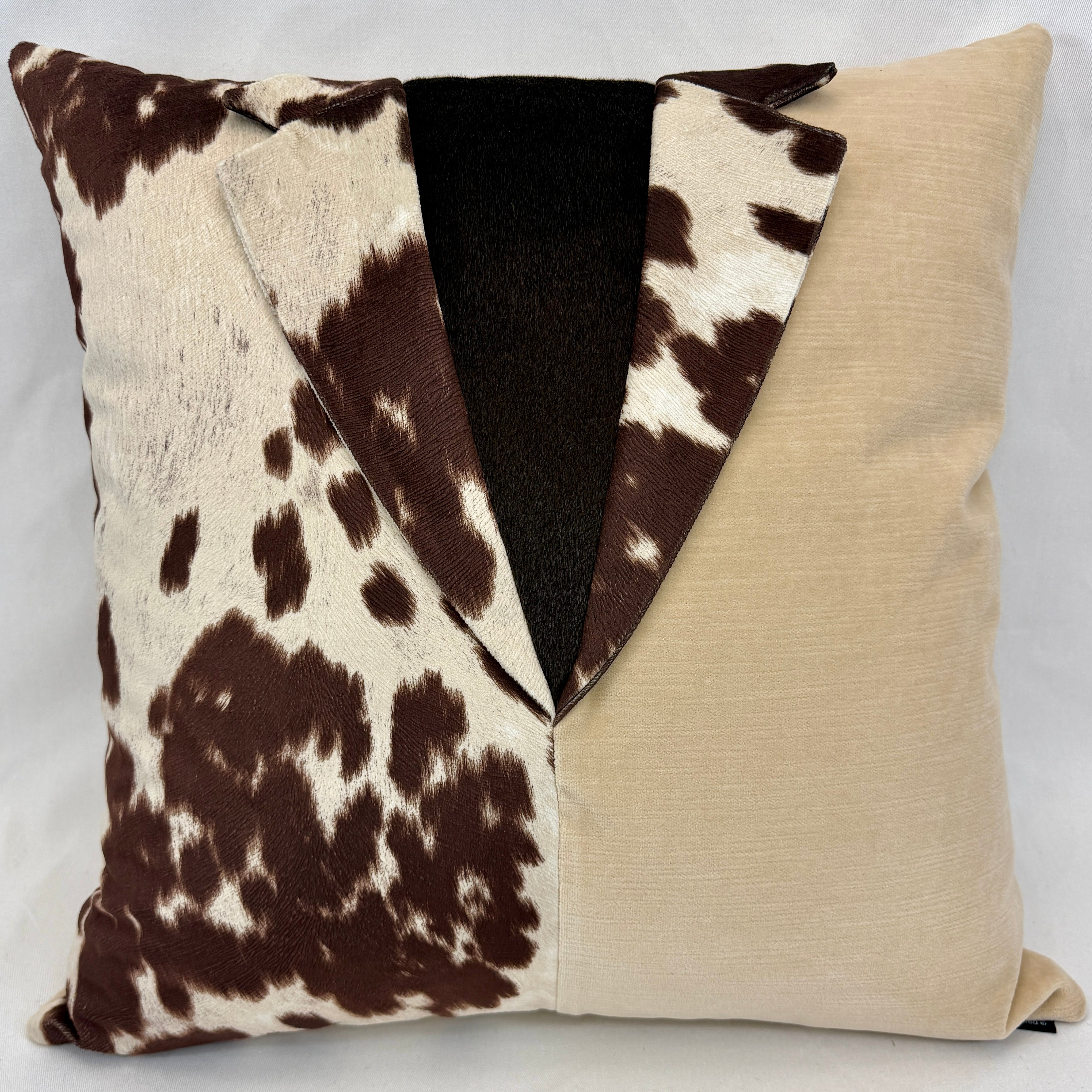 A square decorative throw pillow with a unique split design: one half features a brown and cream cow print, and the other half is a solid beige linen-like fabric. The center is folded over to reveal a dark brown plush lining.