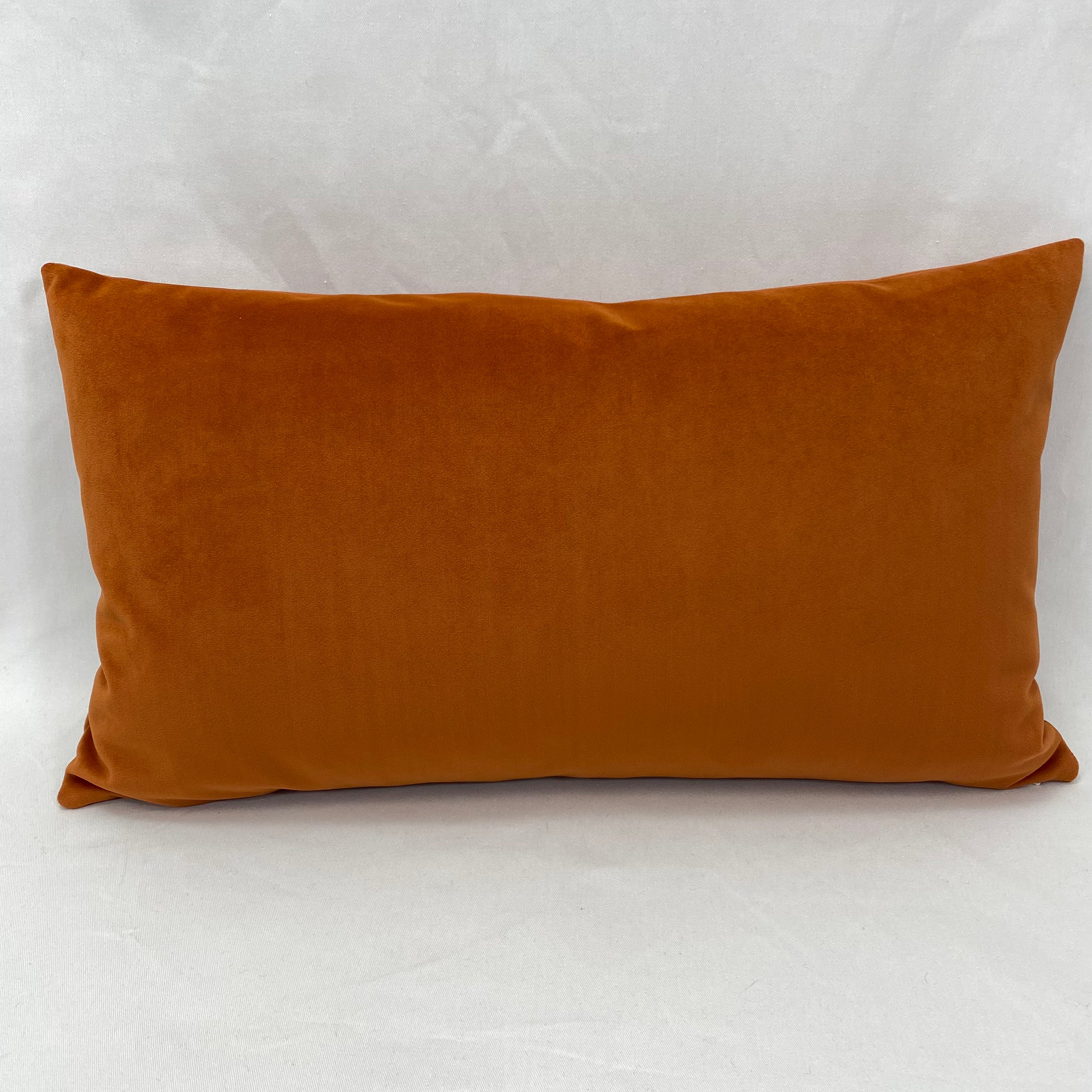 A rectangular lumbar throw pillow in a rich rust-orange velvet fabric, photographed against a neutral light gray backdrop.