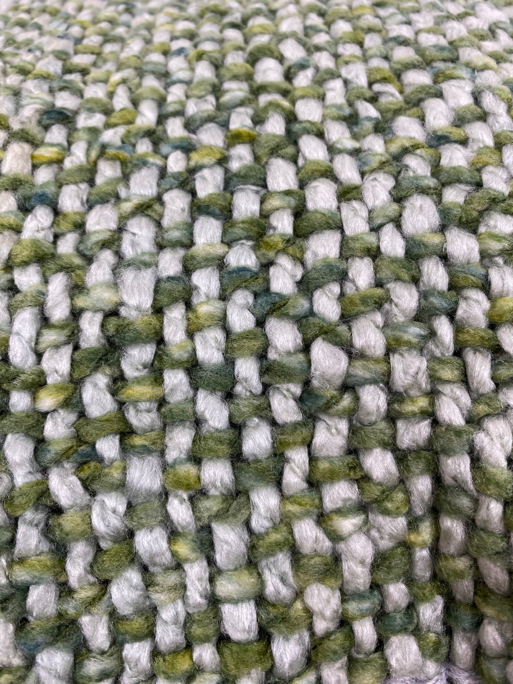 Close-up of a woven textile with a chunky, ribbed texture in variegated shades of sage green, olive, and off-white.