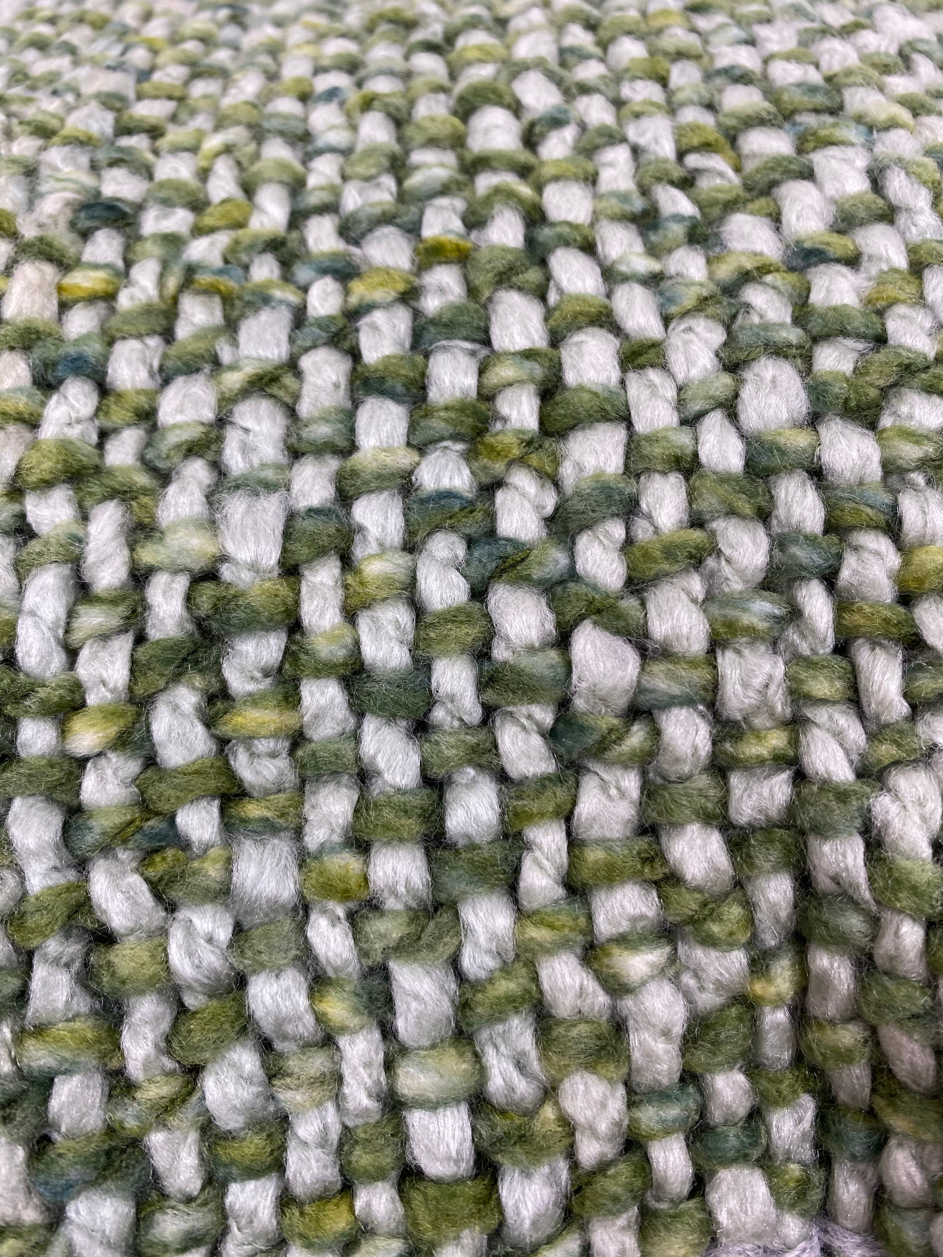 Close-up of a woven textile with a chunky, ribbed texture in variegated shades of sage green, olive, and off-white.