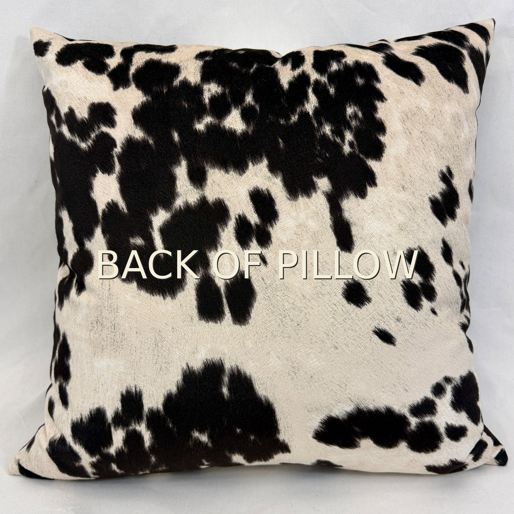 A square throw pillow with a black and cream cowhide pattern, featuring the text 'BACK OF PILLOW' printed across the center, set against a plain light gray background.