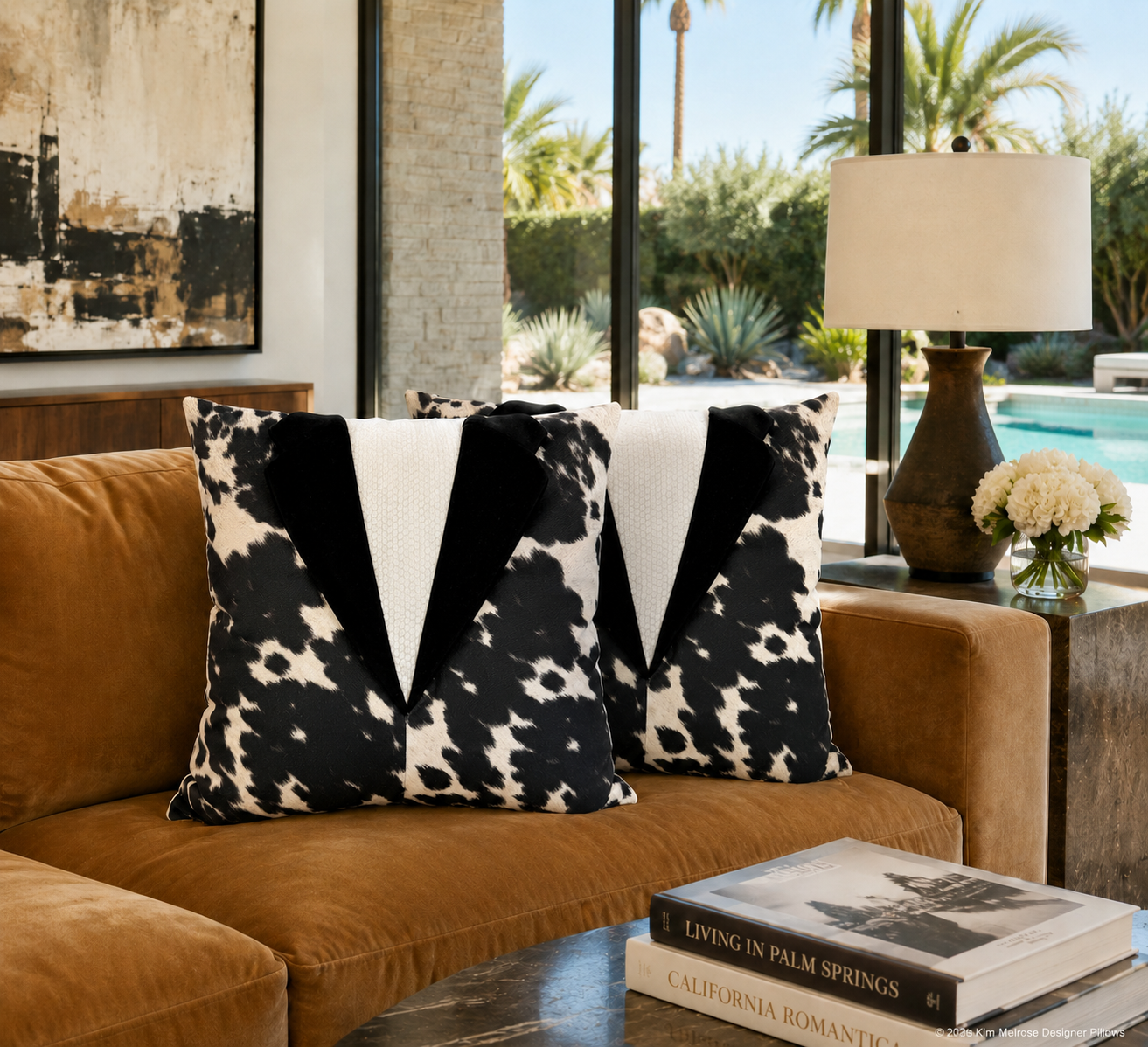 Two decorative throw pillows with a black and white cow-print and bold black V-shaped panels, styled on a brown velvet sofa in a modern living room setting.