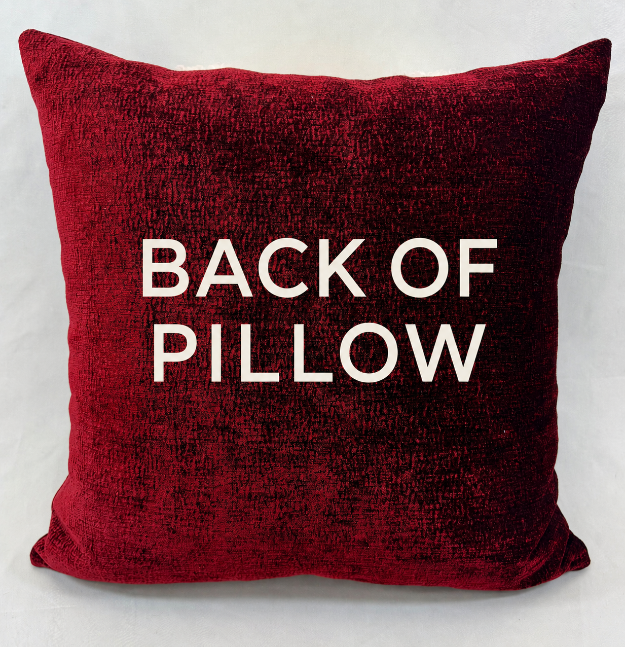 A square red velvet throw pillow with the words 'BACK OF PILLOW' printed in bold white capital letters on the front, set against a light gray background.