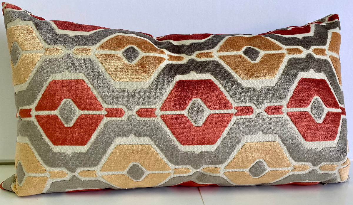 A lumbar pillow with a geometric pattern featuring hexagons in coral, orange, and red colors on a steel grey background.
